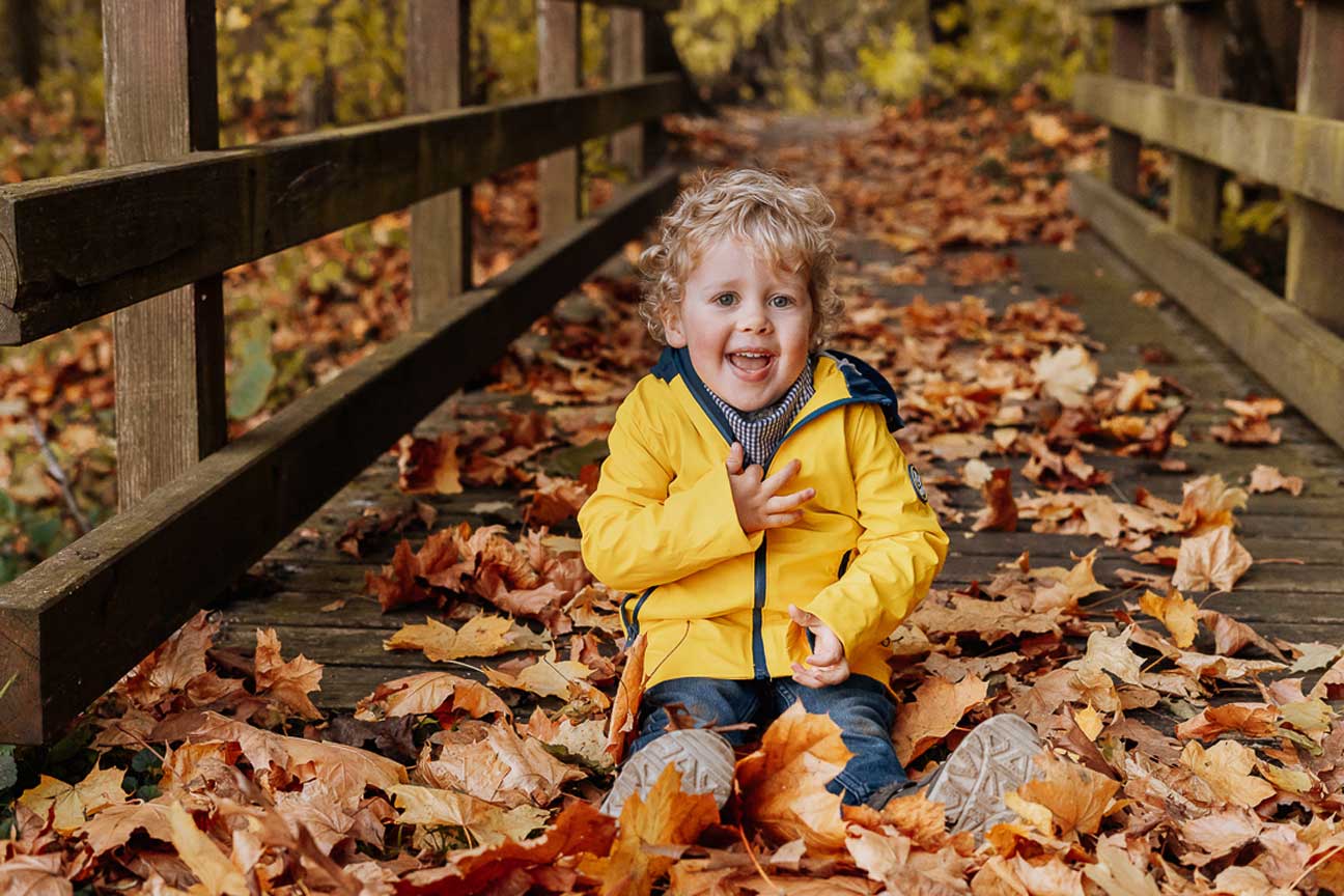 Kind im Herbstlaub auf einer Brücke
